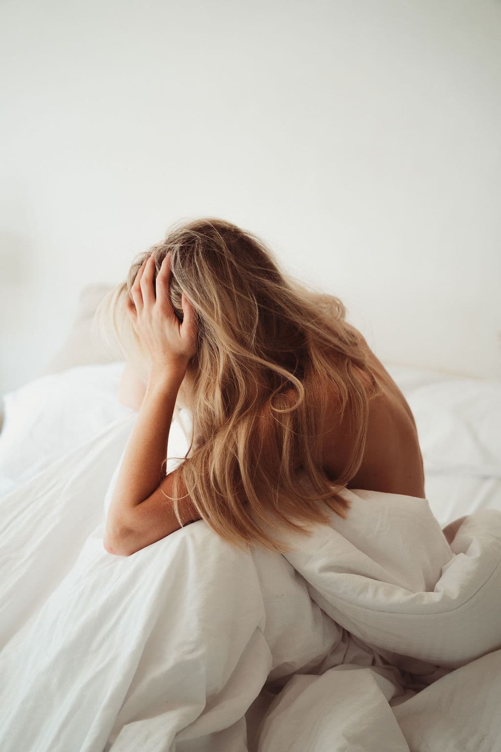 Blonde woman resting her head in her hands on white sheets