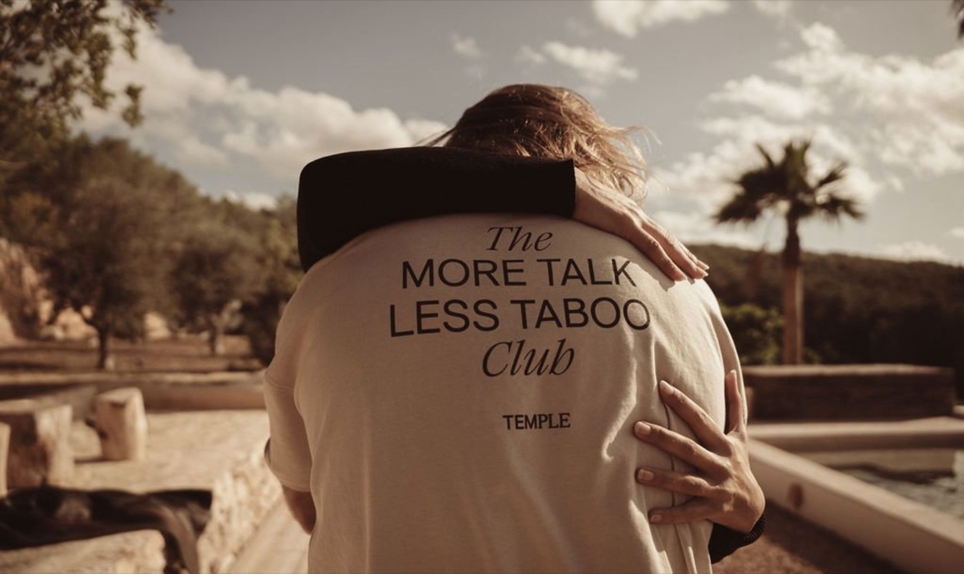 Par som kramas iklädda tröjor med texten “More Talk Less Taboo Club” från Temple