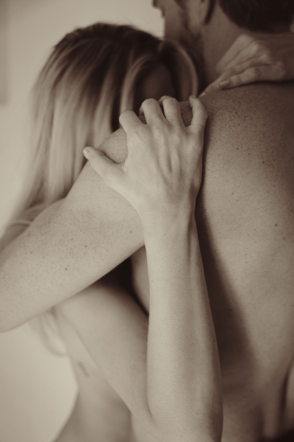 Närbild på en kvinnas hand som griper tag hårt om sin partners axel under en kram, varm sepiaton, ansiktena bortvända