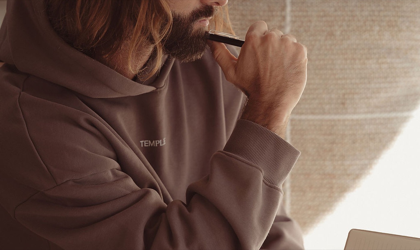 Mann im Temple-Hoodie hält mit Stift und offenem Notizbuch inne, in Gedanken versunken über Intimitätsprobleme und emotionale Nähe