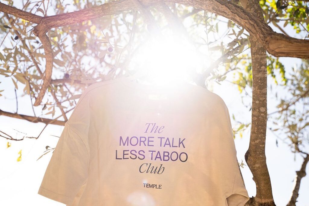 En More Talk Less Taboo Club-tröja som hänger i ett träd i solljus