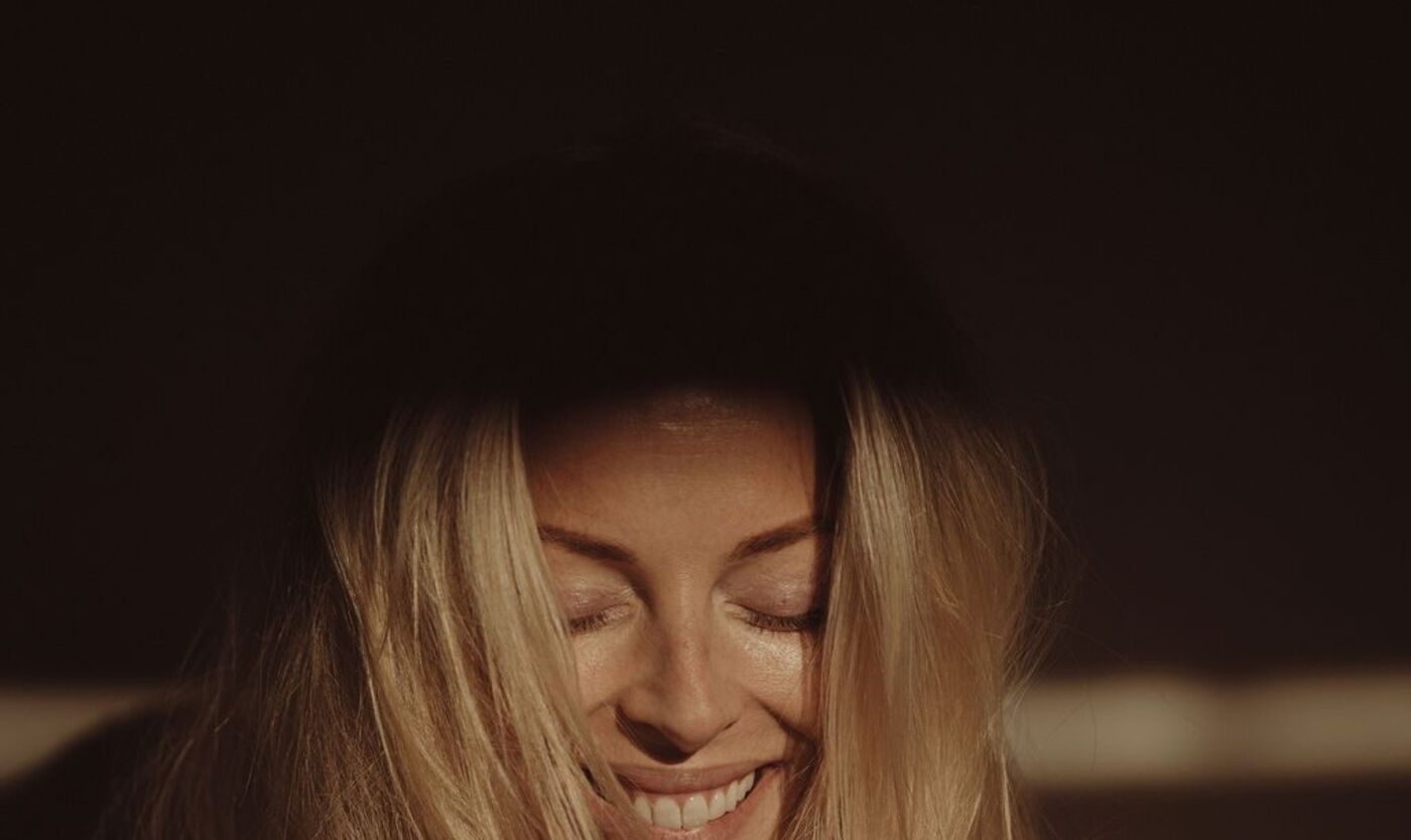 Woman with her eyes closed and a small smile in warm low light, the settled state the method is working toward